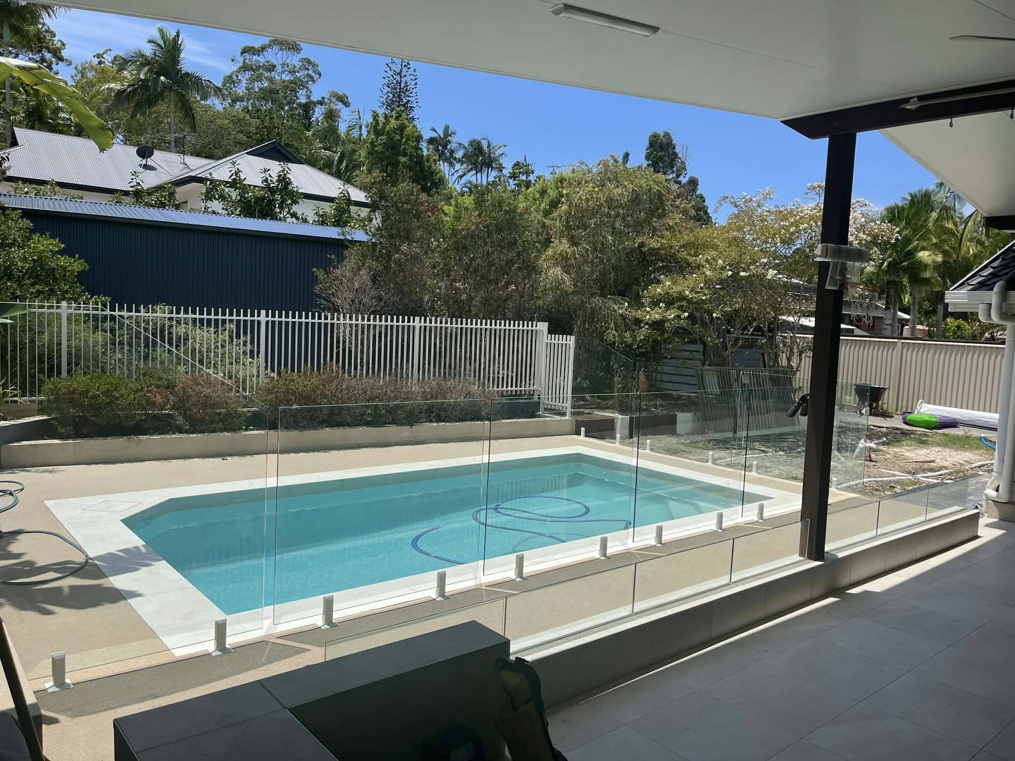 Frameless glass pool fence with white spigots beside a covered patio